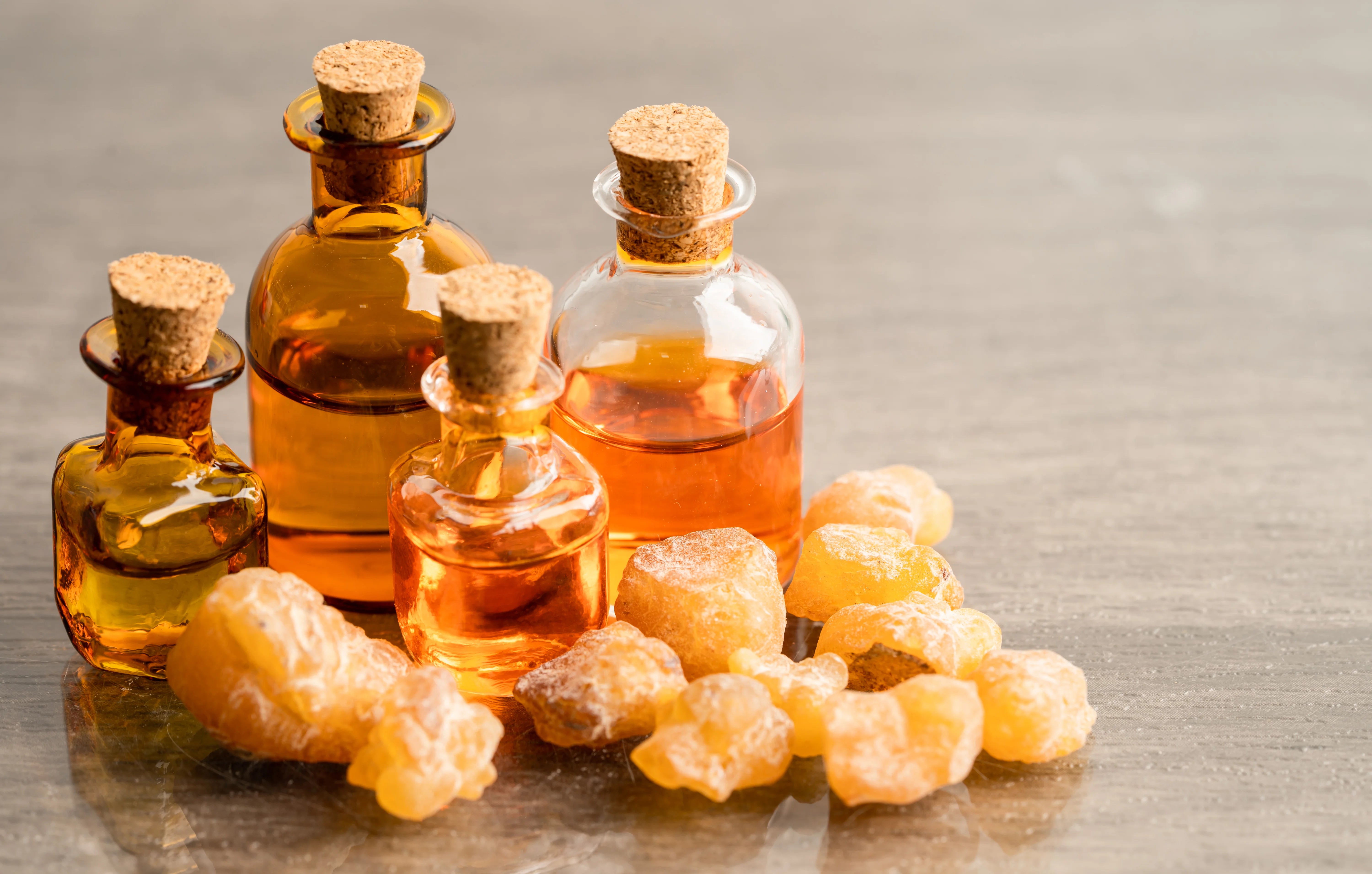Collection of small glass bottles with cork lids and chunks of frankincense resin on a reflective surface.