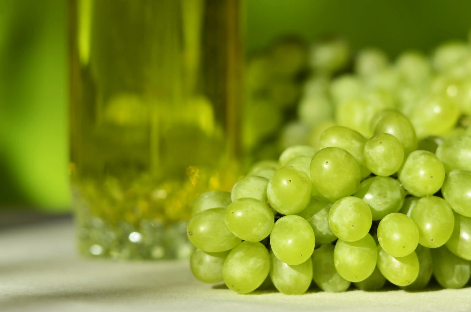 Bottle of grapeseed oil next to a bunch of red grapes on a wooden surface